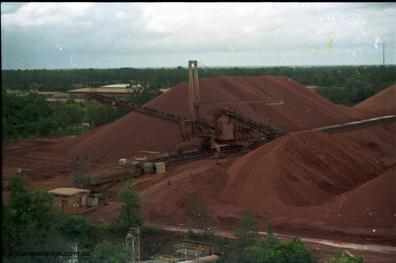 211-03
Weipa, Lorim Point stockpile area viewed from the wharf. A stacker is at the end of the yard belt with the reclaim tunnel for the wharf just visible at the bottom of frame.

