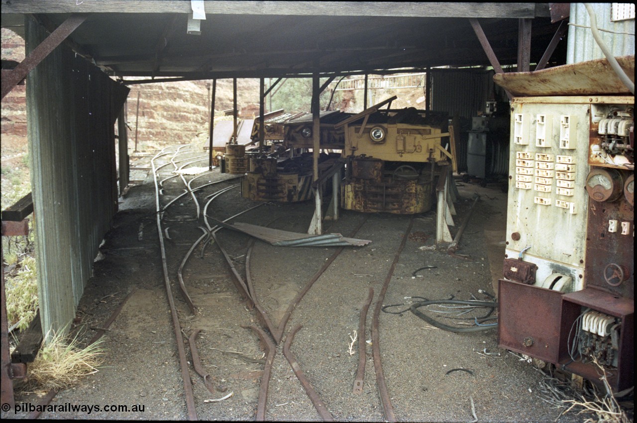 194-25
Wittenoom Gorge, Colonial Mine, asbestos mining remains, view into the loco workshop - battery charging shed, looking south, Mancha haulers with their battery modules on the racks, switchboard at right, with charging transformer visible in the background.
