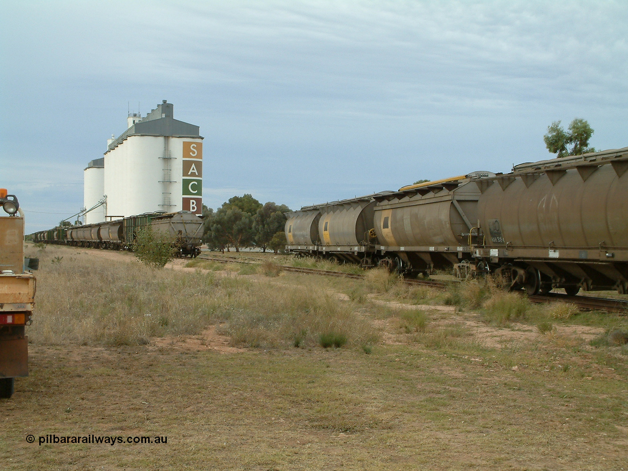 030407 082655
Wudinna, view looking south as the empty rake of bogie grain waggons is shunted into the siding for loading, showing HAN and HCN types of bogie grain hoppers. Concrete SACBH grain complex. 7th April 2003.
Keywords: HAN-type;HCN-type;SAR-Islington-WS;Tulloch-Ltd-NSW;