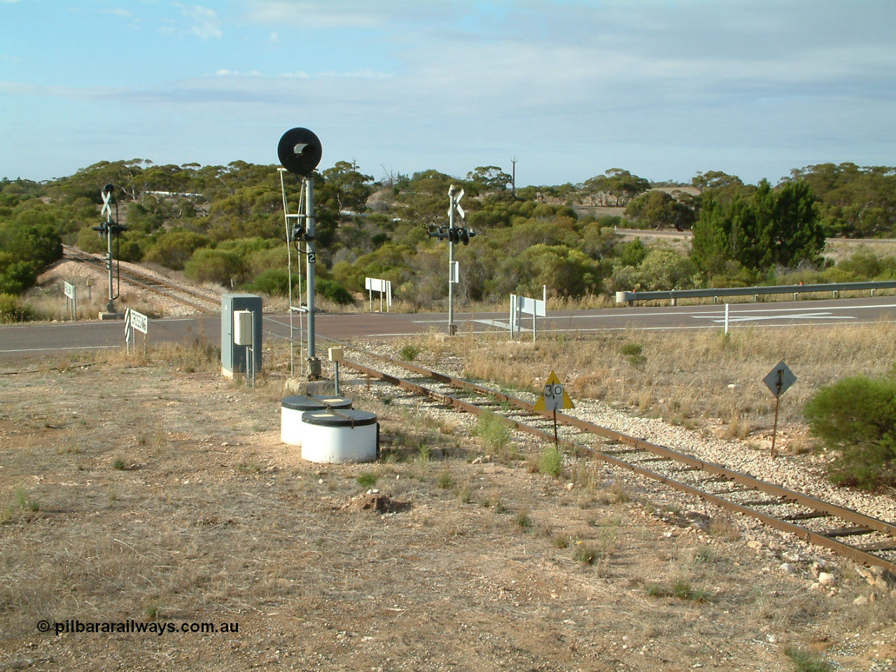 030409 083147
Kyancutta, view of the Eyre Highway grade crossing protected by 'F' type flashing lights, the searchlight signal 2 is one of only three on the Eyre Peninsula system, it is to allow Up trains to enter and shunt the yard.
