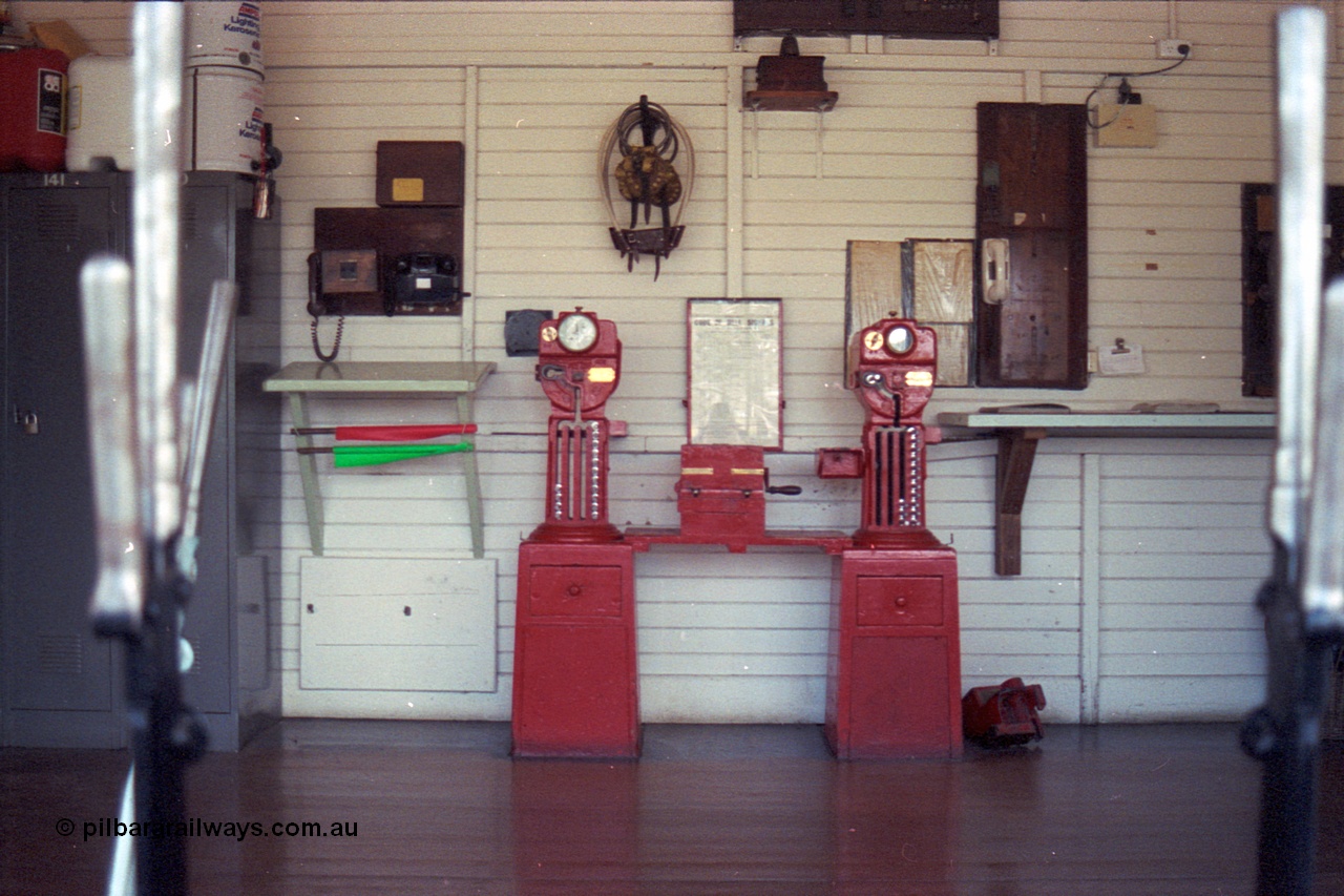 104-15
Buangor, view inside signal box through window, miniature electric staff exchange machines, Buangor to Ararat machine on the left and Trawalla to Buangor machine on the right, control telephones, chart of bell codes, tins of kerosene, exchange hoops and other paraphernalia for running trains in the 19th century.

