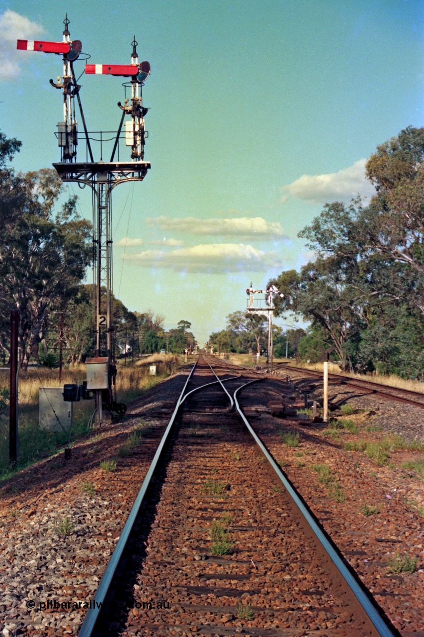 112-00
Violet Town broad gauge track view, looking north, down home semaphore signal post 2, road and signals cleared for up passenger train, calling on semaphores have been removed, standard gauge on the right, March 1994.

