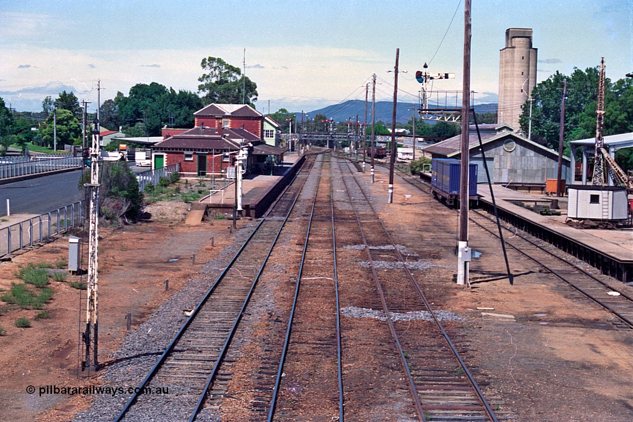 180-12
Wangaratta, rationalised station yard overview looking south from footbridge, removed crossovers from No.2 and 3 to 4 Roads can still be seen in the dirt, also removed Siding A at left of station platform, station building, semaphore signal posts, goods shed and loading platform with slewing derrick crane.
