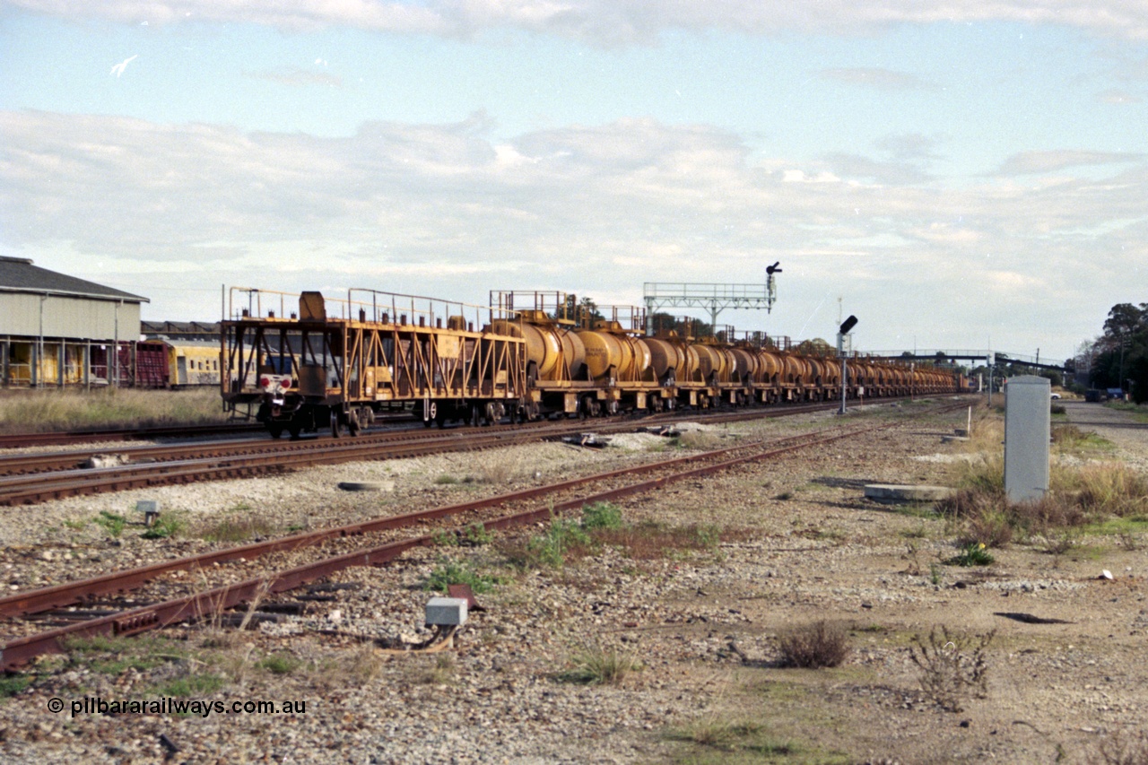 186-03
Midland, trailing view of the standard gauge up Kalgoorlie acid train 428, showing the 28 CSA type tanks on WQH type bogie flat waggons with an WMX type bogie car carrying waggon as the rear barrier waggon, Midland Workshops behind train.
Keywords: WQH-type;CSA-type;WMX-type;