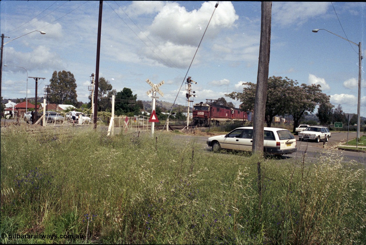 190-23
Cootamundra West, NSW located 431 km from Sydney and the start of the Lake Cargelligo branchline, a Perth bound interstate freight train taking the scenic route, via Cootamundra West, Stockinbingal and Parkes, is about to pass over Yass Road through the manual hand gates behind 81 class locomotive 8159 and a sister unit.
Keywords: 81-class;8159;Clyde-Engineering-Kelso-NSW;EMD;JT26C-2SS;84-1078;