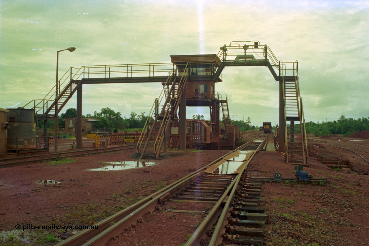 210-04
Weipa, Lorim Point, Comalco rail dump station, view looking towards the workshops, shows inspection walkway and opening for unloading hopper, control cabin, the waggons are discharged on the left track behind the OPEN PIT sign.
