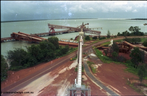 211-00
Weipa, Lorim Point, view from the top of the kaolin storage silos looking north at the kaolin conveyor and ship loader, with red legs and the No.2 bauxite loader straight ahead in the cyclone tie-down position. The bauxite conveyors can be seen passing under the road.
