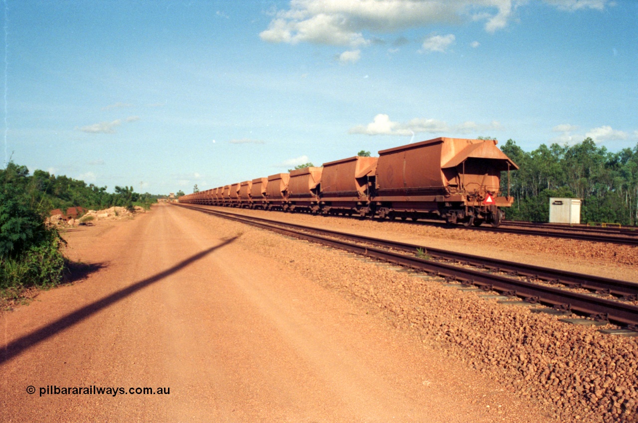 213-07
Weipa, Lorim Point, view looking east from the workshops towards the dump station with a rake of waggons lined up with the two types of aluminium bottom discharge hoppers discernible by the hungry boards fitted to the original type waggons, the control cabin for the dump station can be made out in the distance.
