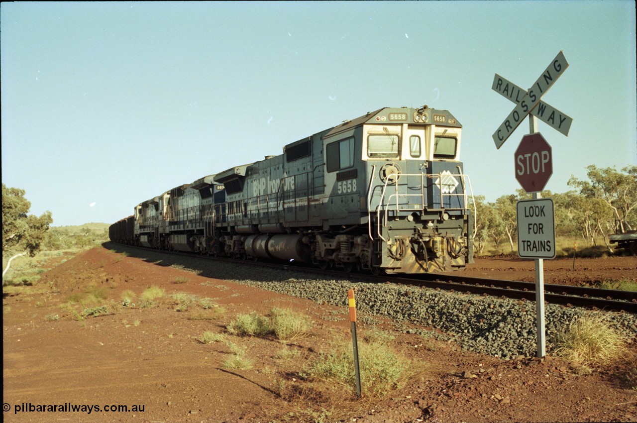 196-03
Yandi Two loaded car side of the loadout balloon loop, BHP Iron Ore CM40-8M or Dash 8 motive power in the form of 5658 'Kakogawa' serial 8412-03 / 94-149 rebuilt by Goninan as GE model CM40-8M from ALCo M636C unit 5480 and two new Goninan built GE CM39-8 units 5630 'Zeus' serial 5831-09 / 88-079 and 5631 'Apollo' serial 5831-10 / 88-080 are the head end power with another two CM40-8M units mid-train. Train length is 240 waggons with a 120/120 split. Yandi Two ore stockpile and pedestal stacker boom tip visible in the background, the loadout operates via gravity and the train travels through a tunnel. May 1998.
Keywords: 5658;Goninan;GE;CM40-8M;8412-03/94-149;rebuild;AE-Goodwin;ALCo;M636C;5480;G6061-1;