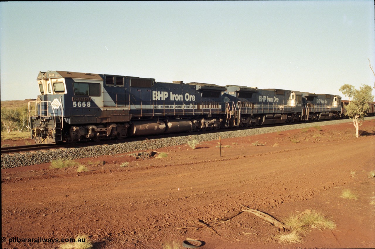 196-04
Yandi Two loaded car side of the loadout balloon loop, BHP Iron Ore CM40-8M or Dash 8 motive power in the form of 5658 'Kakogawa' serial 8412-03 / 94-149 rebuilt by Goninan as GE model CM40-8M from ALCo M636C unit 5480 and two new Goninan built GE CM39-8 units 5630 'Zeus' serial 5831-09 / 88-079 and 5631 'Apollo' serial 5831-10 / 88-080 are the head end power with another two CM40-8M units mid-train. Train length is 240 waggons with a 120/120 split. Yandi Two ore stockpile and pedestal stacker boom tip visible in the background, the loadout operates via gravity and the train travels through a tunnel. May 1998.
Keywords: 5658;Goninan;GE;CM40-8M;8412-03/94-149;rebuild;AE-Goodwin;ALCo;M636C;5480;G6061-1;