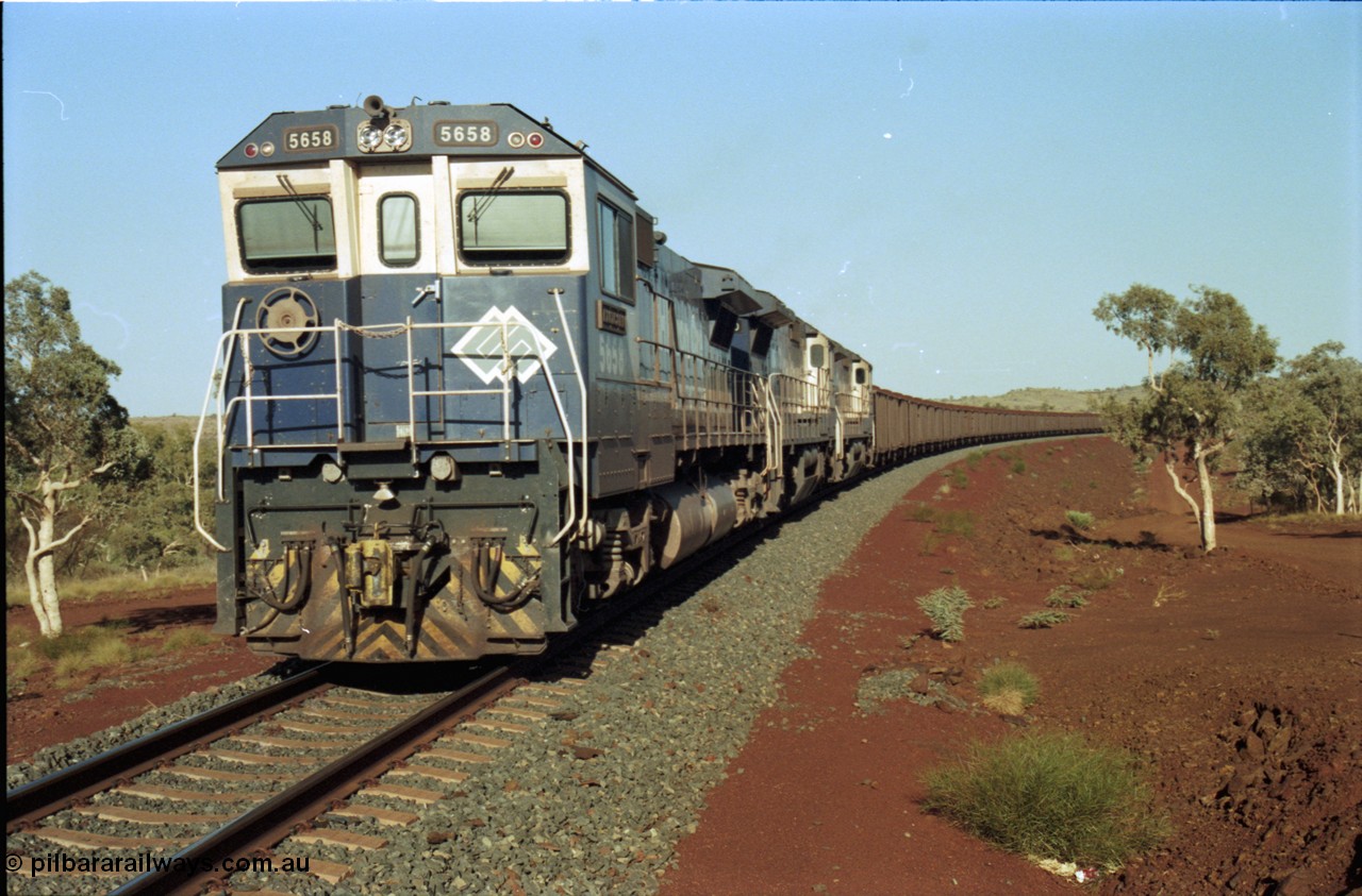 196-11
Yandi Two loaded car side of the loadout balloon loop, BHP Iron Ore CM40-8M or Dash 8 motive power in the form of 5658 'Kakogawa' serial 8412-03 / 94-149 rebuilt by Goninan as GE model CM40-8M from ALCo M636C number 5480 and two new Goninan built GE CM39-8 units 5630 'Zeus' serial 5831-09 / 88-079 and 5631 'Apollo' serial 5831-10 / 88-080 are the head end power with another two CM40-8M units mid-train. Train length is 240 waggons with a 120/120 split. Yandi Two ore stockpile and pedestal stacker boom tip visible in the background, the loadout operates via gravity and the train travels through a tunnel. May 1998.
Keywords: 5658;Goninan;GE;CM40-8M;8412-03/94-149;rebuild;AE-Goodwin;ALCo;M636C;5480;G6061-1;