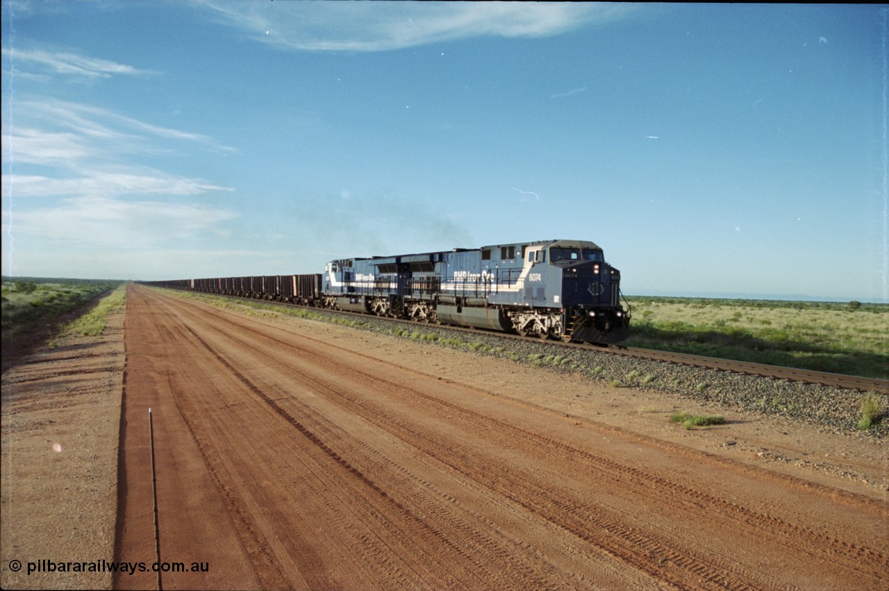 225-19
At the 24.1 km grade crossing on the BHP Newman line, the afternoon departure for Yandi mine heads south behind the standard double General Electric AC6000 units with GE Erie built 6074 serial 51066 leading sister unit 6075 with another AC6000 unit mid-train. This was before the units were named. [url=https://goo.gl/maps/qGkyfiuy6212]GeoData[/url].
Keywords: 6074;GE;AC6000;51066;