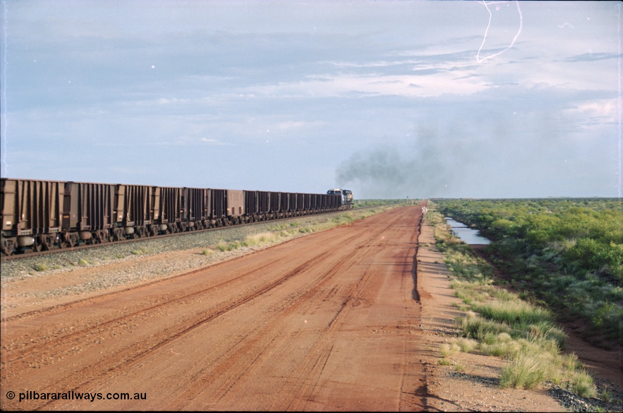 225-23
At the 24.1 km grade crossing on the BHP Newman line, the afternoon departure for Yandi mine heads south behind the standard double General Electric AC6000 units with GE Erie built 6075 serial 51067 second unit to lead sister unit 6074 with another AC6000 unit mid-train. This was before the units were named. [url=https://goo.gl/maps/qGkyfiuy6212]GeoData[/url].
