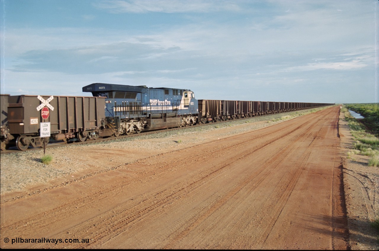 225-24
At the 24.1 km grade crossing on the BHP Newman line, General Electric AC6000 model unit 6073 serial 51065 built at GE Erie is the mid-train remote for the afternoon empty Yandi mine train as it heads south. This was before the units were named. [url=https://goo.gl/maps/qGkyfiuy6212]GeoData[/url].
Keywords: 6073;GE;AC6000;51065;