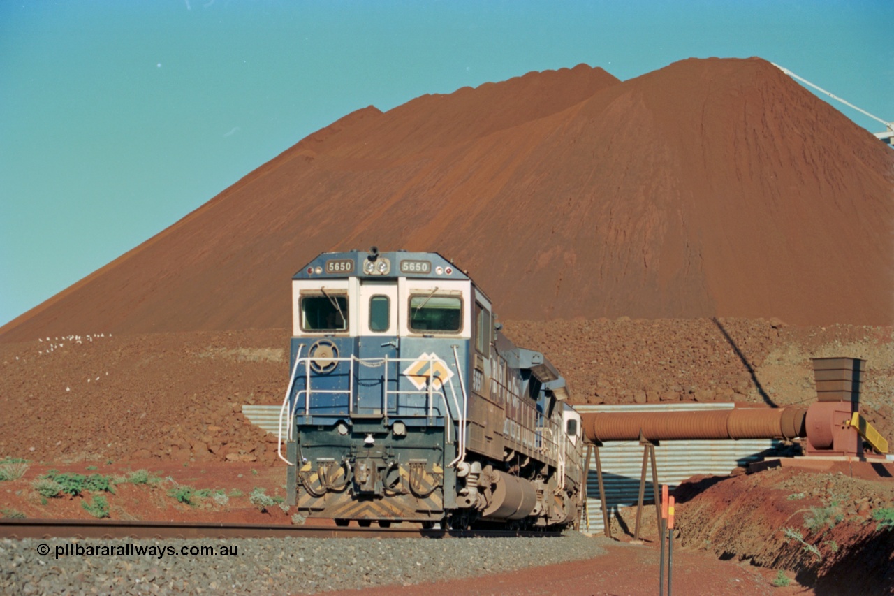 229-20
Yandi Two loadout, looking at the exit portal of the tunnel as Goninan rebuild CM40-8M GE unit 5650 'Yawata' serial 8412-07 / 93-141 drags a loading train through at 1.2 km/h, the massive pile of ore is gravity fed into the waggons via two sets of hydraulic chutes, the original pedestal radial stacker is visible above the ore along with the extraction fan. [url=https://goo.gl/maps/jmtnauf76Zq]GeoData[/url].
Keywords: 5650;Goninan;GE;CM40-8M;8412-07/93-141;rebuild;AE-Goodwin;ALCo;M636C;5481;G6061-2;