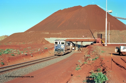 229-19
Yandi Two loadout, looking at the exit portal of the tunnel as Goninan rebuild CM40-8M GE unit 5650 'Yawata' serial 8412-07 / 93-141 drags a loading train through at 1.2 km/h, the massive pile of ore is gravity fed into the waggons via two sets of hydraulic chutes, the original pedestal radial stacker is visible above the ore along with the extraction fan. [url=https://goo.gl/maps/jmtnauf76Zq]GeoData[/url].
Keywords: 5650;Goninan;GE;CM40-8M;8412-07/93-141;rebuild;AE-Goodwin;ALCo;M636C;5481;G6061-2;