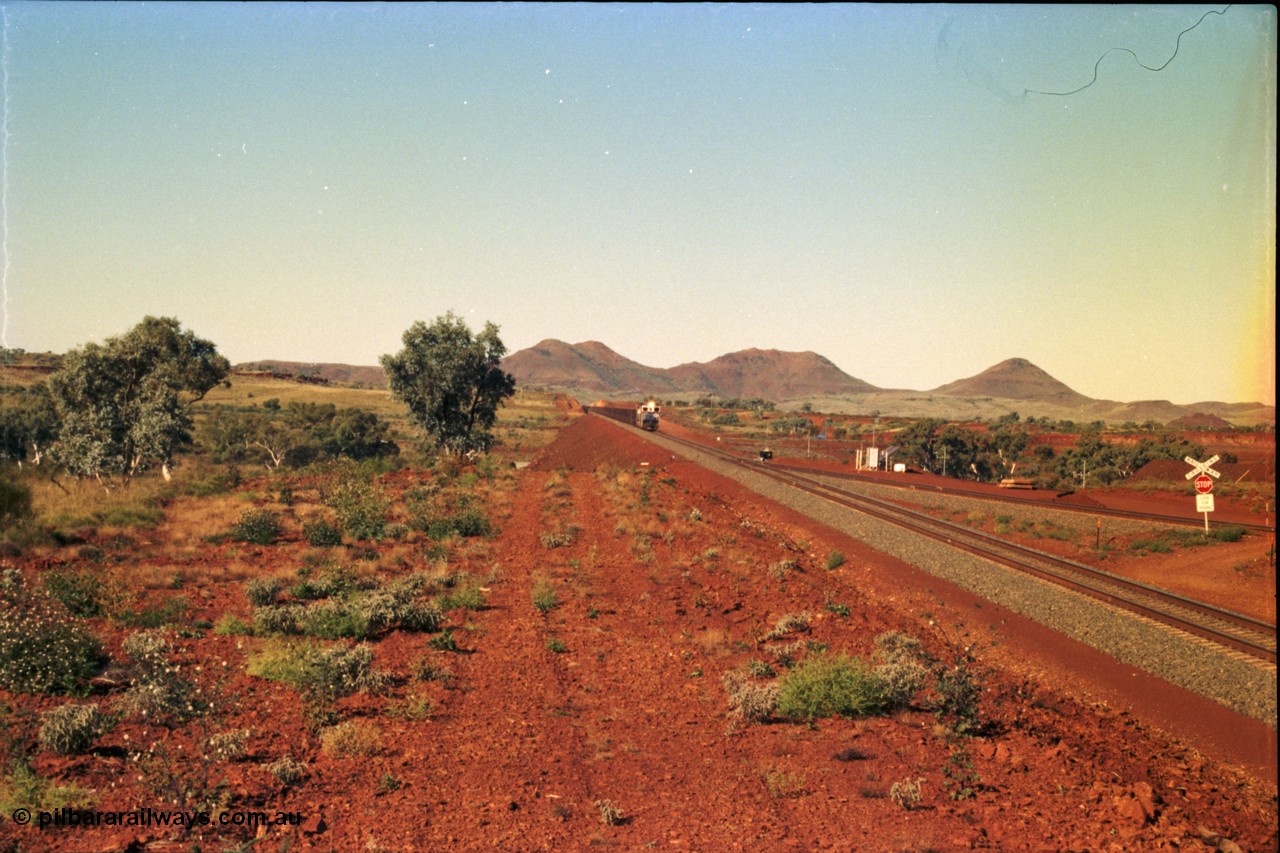 230-01
Yandi Two switch looking east with the Three Sisters forming the background. Empty BHP train heading for the balloon loop for loading, grade crossing is the YT 311.5 km. Geodata [url=https://goo.gl/maps/DcycDGojcBt] -22.713725, 119.055762 [/url].
