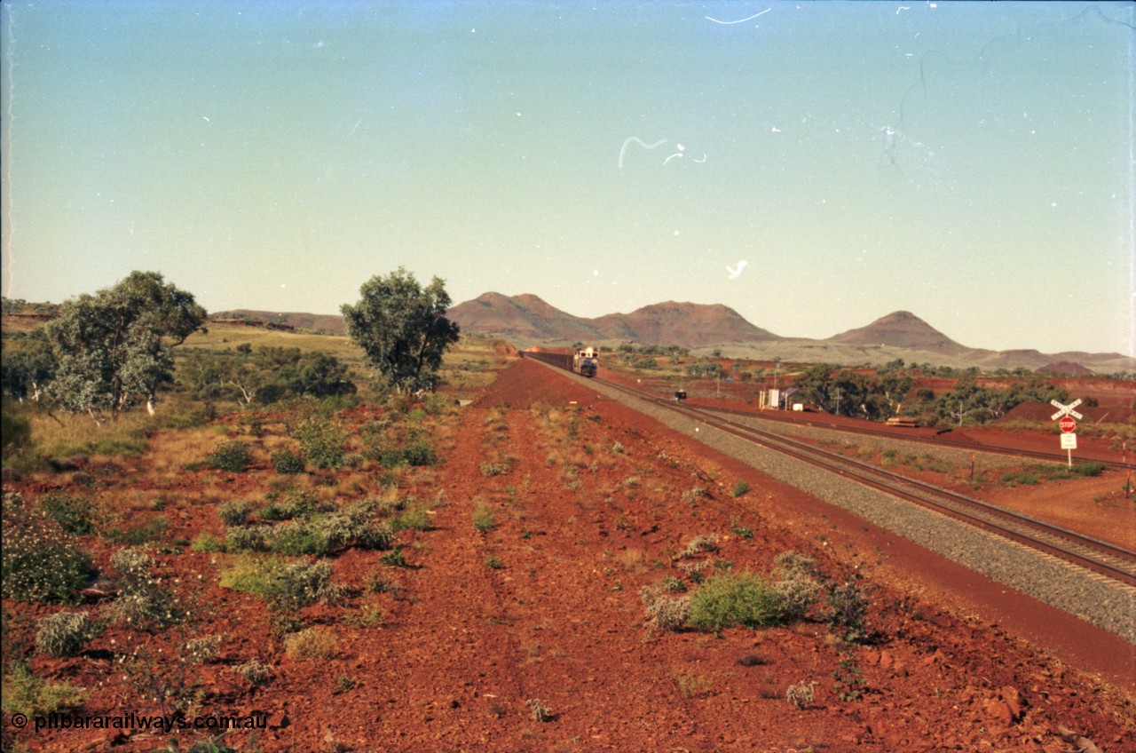 230-02
Yandi Two switch looking east with the Three Sisters forming the background. Empty BHP train heading for the balloon loop for loading, grade crossing is the YT 311.5 km. Geodata [url=https://goo.gl/maps/DcycDGojcBt] -22.713725, 119.055762 [/url].
