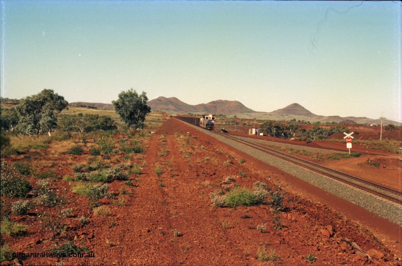 230-04
Yandi Two switch looking east with the Three Sisters forming the background. Empty BHP train heading for the balloon loop for loading, grade crossing is the YT 311.5 km. Geodata [url=https://goo.gl/maps/DcycDGojcBt] -22.713725, 119.055762 [/url].
