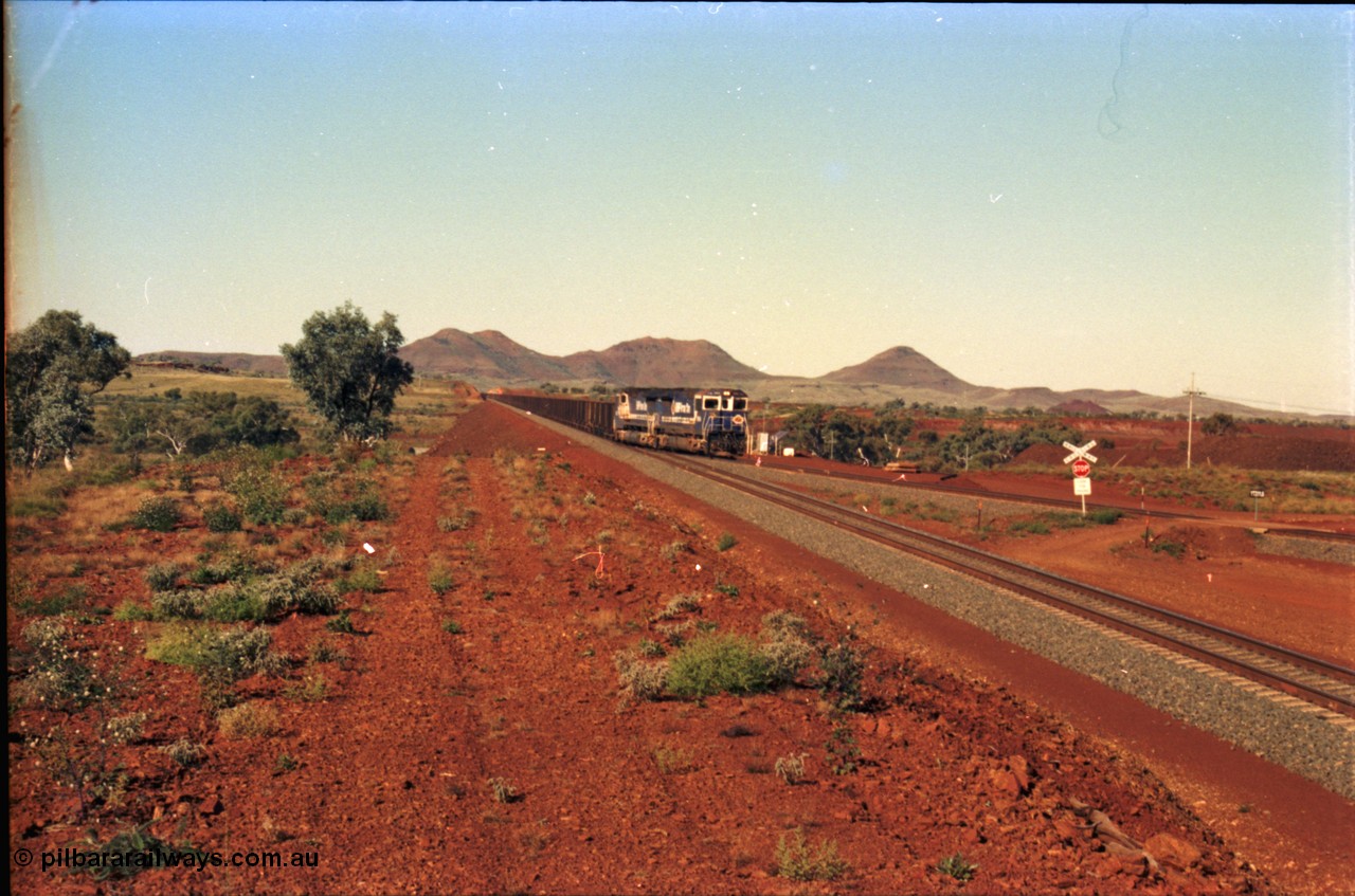 230-06
Yandi Two switch looking east with the Three Sisters forming the background. Empty BHP train heading for the balloon loop for loading, grade crossing is the YT 311.5 km. Geodata [url=https://goo.gl/maps/DcycDGojcBt] -22.713725, 119.055762 [/url].
