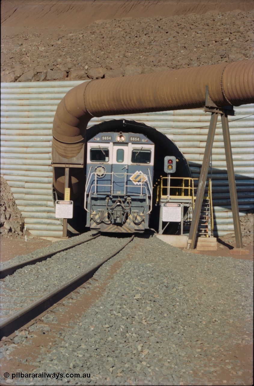 230-12
Yandi Two load-out tunnel exit side portal, Goninan rebuild GE CM40-8M model 5654 'Kashima' serial 8412-11/93-145 creeps out of the tunnel as its train is loaded at 1.2 km/h. The livery is the marigold version of the BHP Australia logo. The pipe is for the dust extraction system. Geodata [url=https://goo.gl/maps/h68ia1caJvL2] -22.718338, 119.039909 [/url].
Keywords: 5654;Goninan;GE;CM40-8M;8412-11/93-145;rebuild;Comeng-NSW;ALCo;M636C;5493;C6084-9;