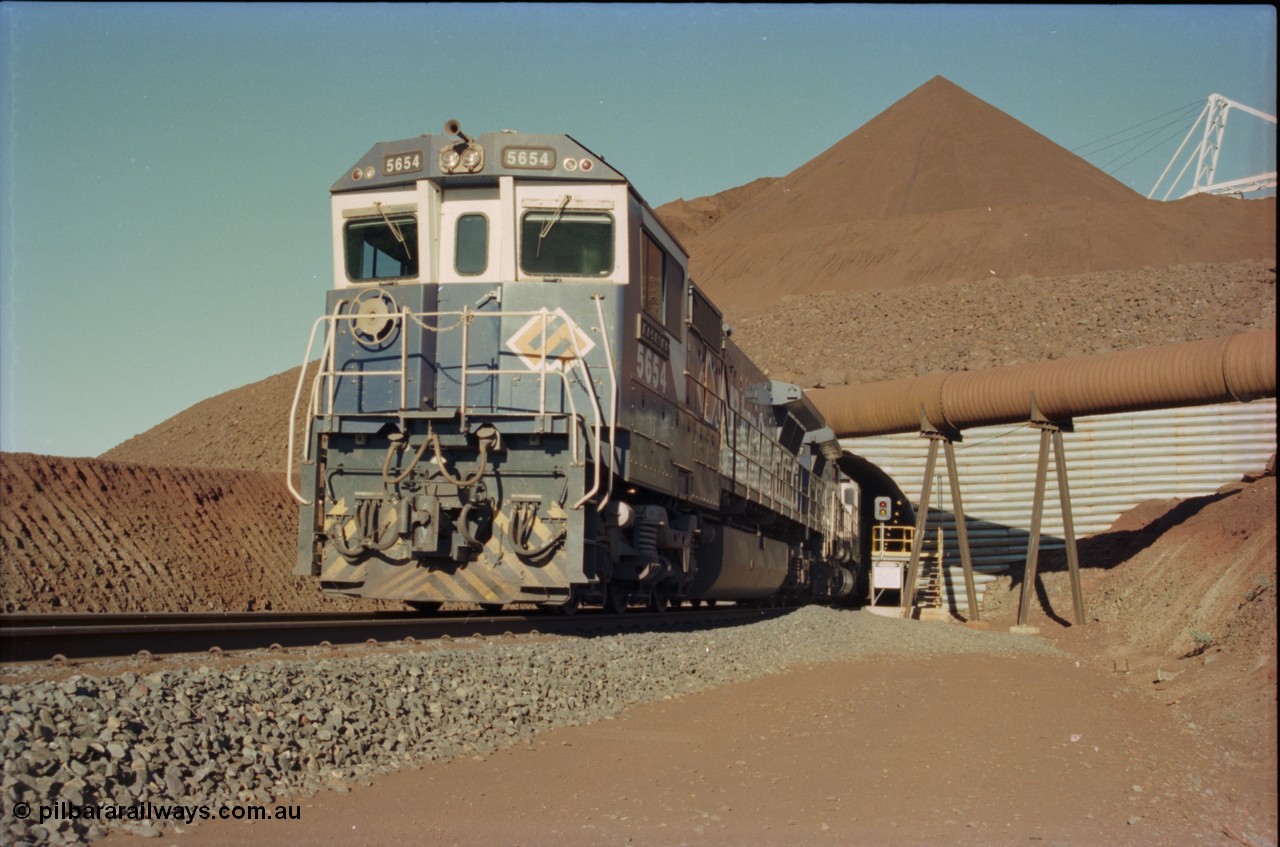 230-17
Yandi Two load-out tunnel exit side portal, Goninan rebuild GE CM40-8M model 5654 'Kashima' serial 8412-11/93-145 leads a loading train 1.2 km/h. The ore stockpile and pedestal stacker are visible. The livery is the marigold version of the BHP Australia logo. Geodata [url=https://goo.gl/maps/h68ia1caJvL2] -22.718338, 119.039909 [/url].
Keywords: 5654;Goninan;GE;CM40-8M;8412-11/93-145;rebuild;Comeng-NSW;ALCo;M636C;5493;C6084-9;