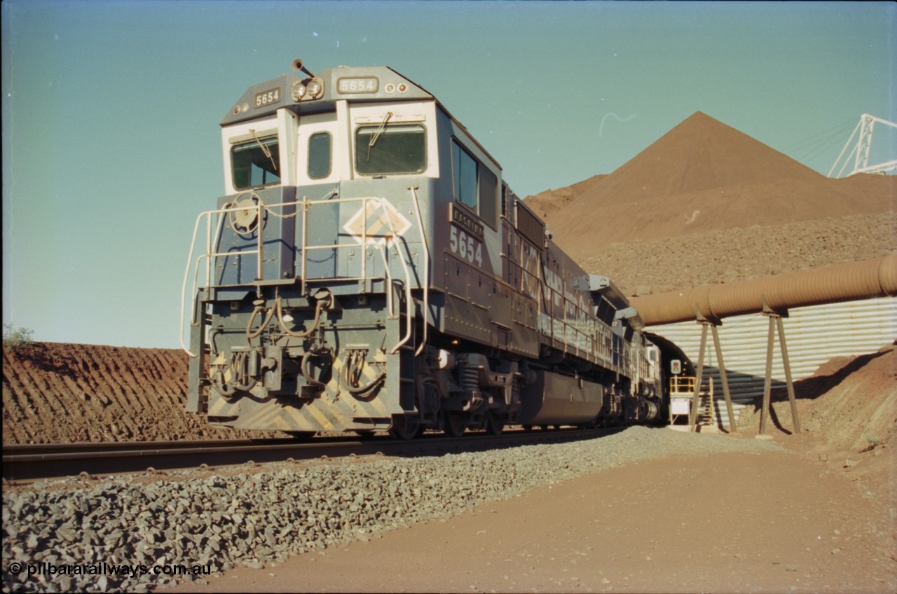 230-18
Yandi Two load-out tunnel exit side portal, Goninan rebuild GE CM40-8M model 5654 'Kashima' serial 8412-11/93-145 leads a loading train 1.2 km/h. The ore stockpile and pedestal stacker are visible. The livery is the marigold version of the BHP Australia logo. Geodata [url=https://goo.gl/maps/h68ia1caJvL2] -22.718338, 119.039909 [/url].
Keywords: 5654;Goninan;GE;CM40-8M;8412-11/93-145;rebuild;Comeng-NSW;ALCo;M636C;5493;C6084-9;