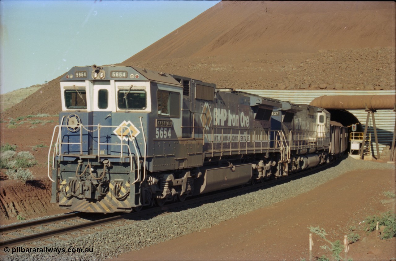 230-22
Yandi Two load-out tunnel exit side portal, Goninan rebuild GE CM40-8M model 5654 'Kashima' serial 8412-11/93-145 leads a loading train 1.2 km/h. The livery is the marigold version of the BHP Australia logo. Geodata [url=https://goo.gl/maps/h68ia1caJvL2] -22.718338, 119.039909 [/url].
Keywords: 5654;Goninan;GE;CM40-8M;8412-11/93-145;rebuild;Comeng-NSW;ALCo;M636C;5493;C6084-9;