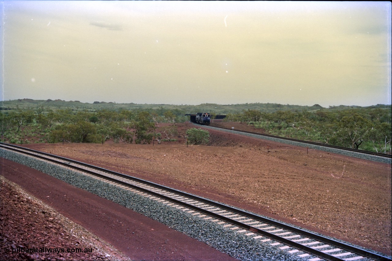 232-04
Yandi Two, view west from near the 311.6 km grade crossing, train can be seen loading on the right. February 1997. [url=https://goo.gl/maps/3tst5WV949N2]GeoData[/url].
