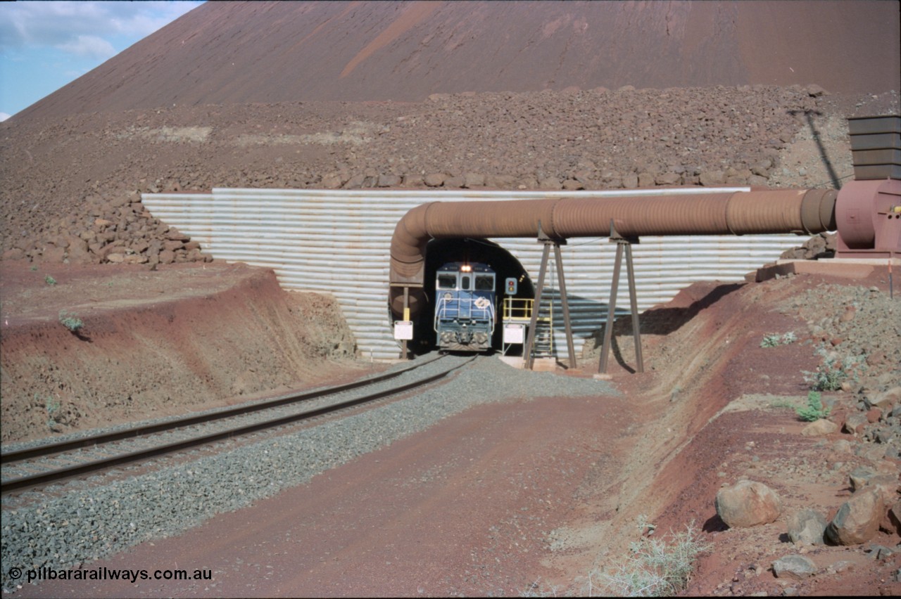 233-07
Yandi Two exit portal or loaded car side of load-out tunnel, the Yandi Two load-out has two load-out stations or vaults to allow to different products to be loaded. Only one vault is used at a time. A loading train lead by BHP Iron Ore's Goninan rebuild CM40-8M GE unit 5650 'Yawata' serial 8412-07 / 93-141 as it drags the train through at 1.2 km/h. [url=https://goo.gl/maps/RgJfYGtPXb52]GeoData[/url].
