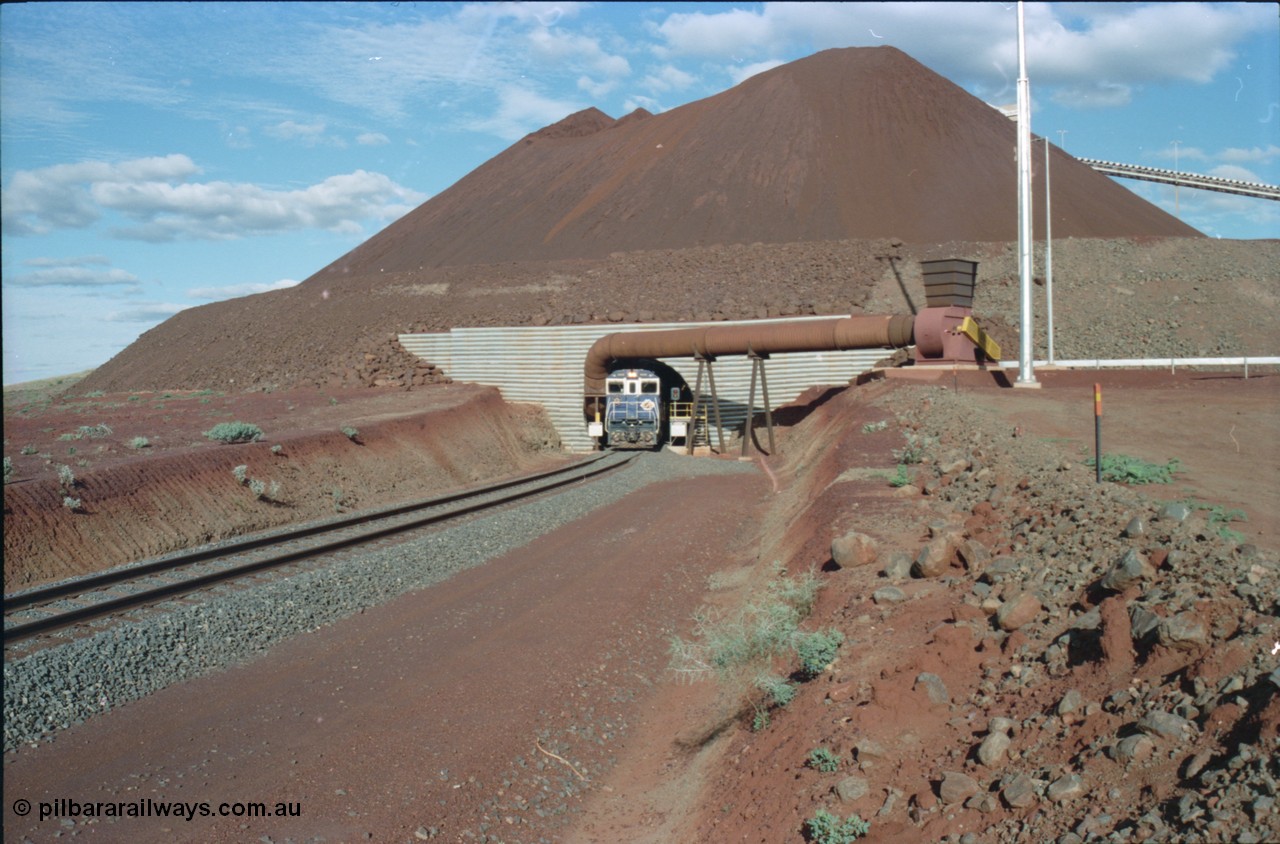 233-10
Yandi Two exit portal or loaded car side of load-out tunnel, the Yandi Two load-out has two load-out stations or vaults to allow to different products to be loaded. Only one vault is used at a time. A loading train lead by BHP Iron Ore's Goninan rebuild CM40-8M GE unit 5650 'Yawata' serial 8412-07 / 93-141 as it drags the train through at 1.2 km/h. [url=https://goo.gl/maps/RgJfYGtPXb52]GeoData[/url].
Keywords: 5650;Goninan;GE;CM40-8M;8412-07/93-141;rebuild;AE-Goodwin;ALCo;M636C;5481;G6061-2;