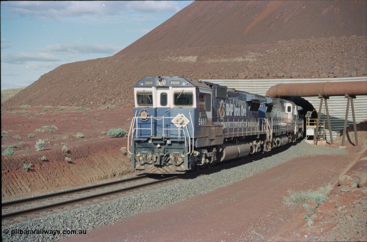 233-15
Yandi Two exit portal or loaded car side of load-out tunnel, the Yandi Two load-out has two load-out stations or vaults to allow to different products to be loaded. Only one vault is used at a time. A loading train lead by BHP Iron Ore's Goninan rebuild CM40-8M GE unit 5650 'Yawata' serial 8412-07 / 93-141 as it drags the train through at 1.2 km/h with assistance from two sister units. [url=https://goo.gl/maps/RgJfYGtPXb52]GeoData[/url].
Keywords: 5650;Goninan;GE;CM40-8M;8412-07/93-141;rebuild;AE-Goodwin;ALCo;M636C;5481;G6061-2;