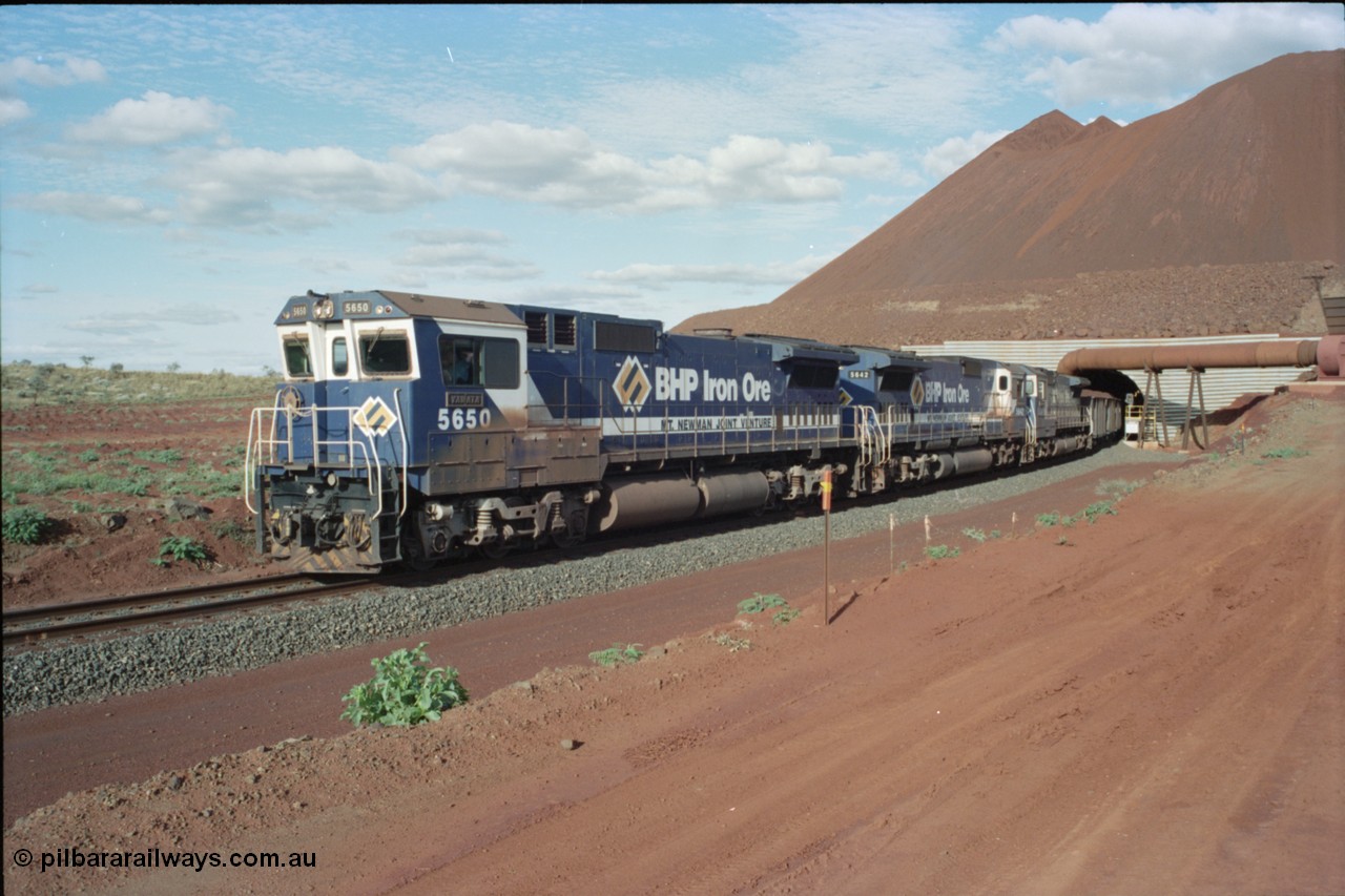 233-20
Yandi Two exit portal or loaded car side of load-out tunnel, the Yandi Two load-out has two load-out stations or vaults to allow to different products to be loaded. Only one vault is used at a time. A loading train lead by BHP Iron Ore's Goninan rebuild CM40-8M GE unit 5650 'Yawata' serial 8412-07 / 93-141 as it drags the train through at 1.2 km/h with assistance from two sister units. [url=https://goo.gl/maps/RgJfYGtPXb52]GeoData[/url].
Keywords: 5650;Goninan;GE;CM40-8M;8412-07/93-141;rebuild;AE-Goodwin;ALCo;M636C;5481;G6061-2;