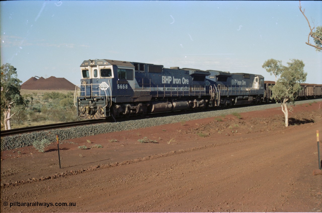 234-26
Yandi Two, BHP Iron Ore Goninan rebuild CM40-8M GE unit 5658 'Kakogawa' serial 8412-03 / 94-149 on the front of a 240 waggon loaded train, this configuration was trialled for a time with two Dash 8 locos, 120 waggons, Dash 8, 120 waggons and Dash 8. View looking from 5658 back to the ore stockpile at the loadout. Circa 1998.
Keywords: 5658;Goninan;GE;CM40-8M;8412-03/94-149;rebuild;AE-Goodwin;ALCo;M636C;5480;G6061-1;