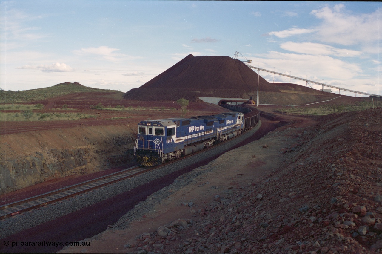 239-32
Yandi Two, train loading is under way with a pair of Goninan rebuild units, CM40-8MEFI unit 5668 'Dunkirk' serial 8412-01/95-159 and CM40-8M unit 5644 'Kangan' serial 8281-09/92-133 with the Yandi Fines stockpile and feed conveyor and pedestal stacker visible.
