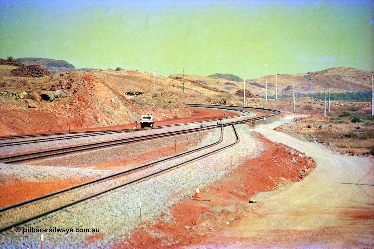 246-05
Cape Lambert, yard view of the then new extension to the south for the West Angelas mine was coming on stream, the just visible siding (rejoining) on the far left will become a compressor waggon holding road, the 6 km and Boat Beach Rd grade crossing are around the corner to the left. Closest to the camera is the extended No. 1 Road which becomes the Empty Car Line from car dumper one for the Deepdale traffic. Next is the original line or Mainline and the third line across is the Loaded Car Line for the West Angelas traffic to the new car dumper 2. 22nd May 2002.
