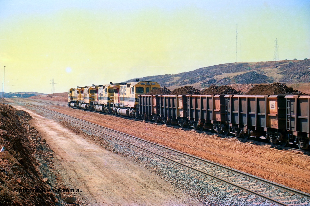 246-28
Cape Lambert, a Robe River loaded Deepdale train rolls along the mainline behind the standard quad Dash 8 power with 202 waggons with newly extended roads either side of it. In the distance can be seen are the railway workshops. 22nd May 2002.
