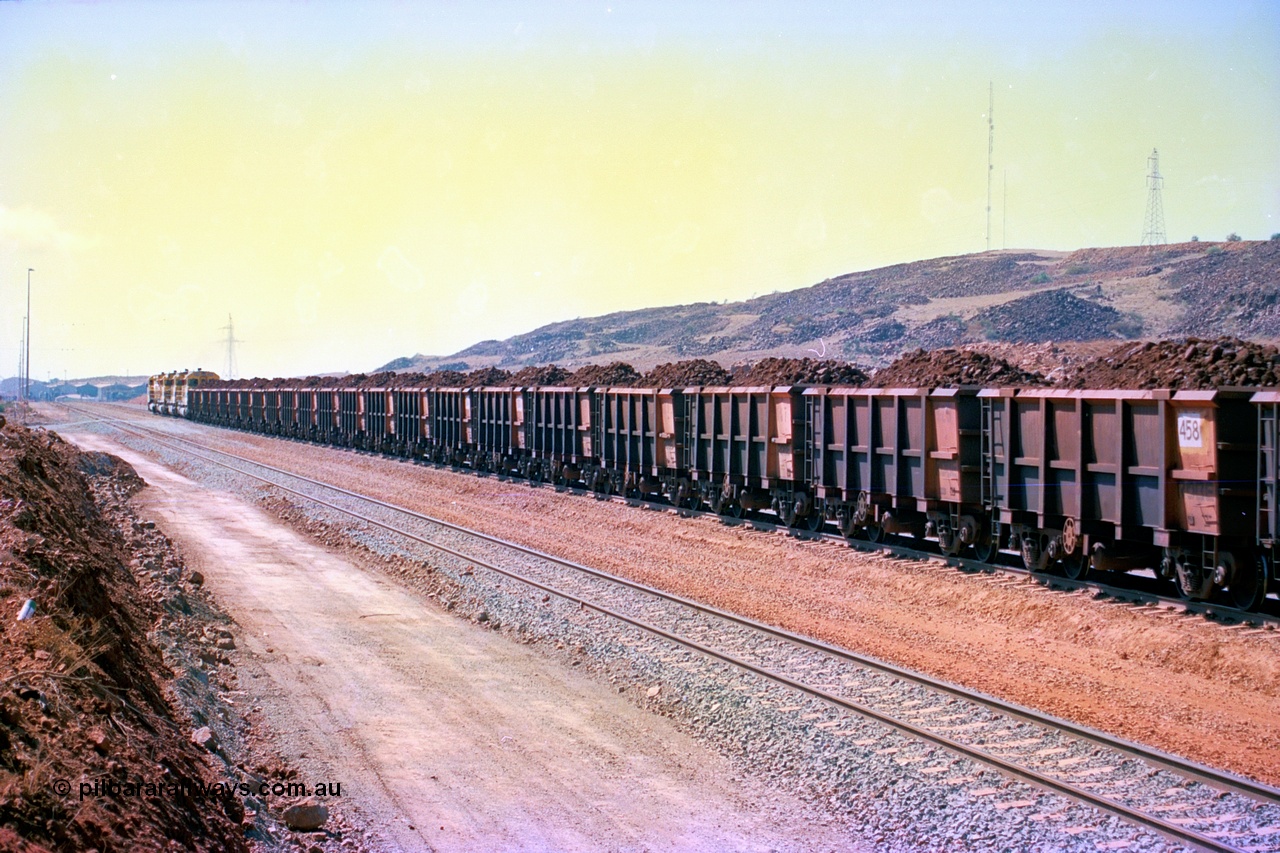 246-35
Cape Lambert, a Robe River loaded Deepdale train rolls along the mainline behind the standard quad Dash 8 power with 202 waggons which are a mix of builds from Nippon Sharyo Japan and Tomlinson Steel and Centurion Industries both WA companies. The ore is a ROM product and will be dumped over the gyratory crusher to be correctly sized. The newly extended roads can be seen either side of the train and in the distance can be seen are the railway workshops. 22nd May 2002.
