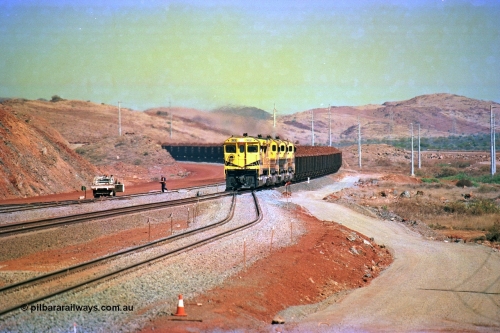 246-12
Cape Lambert, yard view of the then new extension to the south for the West Angelas mine was coming on stream as a Robe River loaded Deepdale train arrives on the main behind the standard quad Dash 8 power with 202 waggons, the just visible siding (rejoining) on the far left will become a compressor waggon holding road, the 6 km and Boat Beach Rd grade crossing are around the corner to the left. Closest to the camera is the extended No. 1 Road which becomes the Empty Car Line from car dumper one for the Deepdale traffic. Next is the original line or Mainline and the third line across is the Loaded Car Line for the West Angelas traffic to the new car dumper 2. 22nd May 2002.
