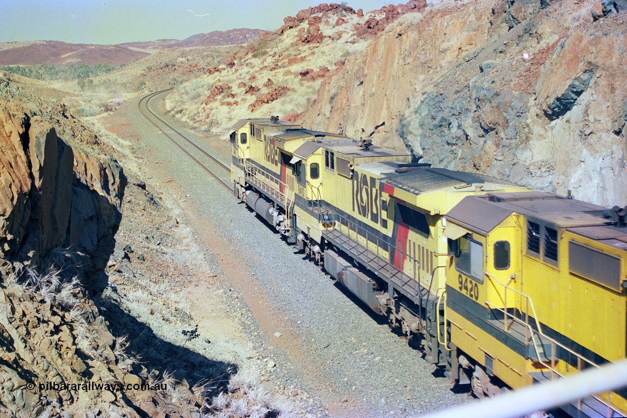 247-33
Near Cooya Pooya at the 37.5 km on the Robe River Cape Lambert line an empty train passes under the town water supply pipeline and pass through Lockyer Gap behind the standard Robe power of quad CM40-8M or Dash 8 locomotives led by 9425 which is a Goninan WA ALCo to GE rebuild CM40-8M with serial 6266-8 / 89-85 from August 1989 and was originally an AE Goodwin built M636 ALCo serial C-6041-4 new for Mt Newman Mining (later BHP Iron Ore) in April 1970 and numbered 5468, sold to Robe and delivered by road 17th August 1982, compare to second unit 9410 with a Comeng style large flat fuel tank. Location is [url=https://goo.gl/maps/nLyndU6bg2HA5SZX6]here[/url].22nd May 2002.
Keywords: 9410;Goninan;GE;CM40-8M;2160-03/96-202;rebuild;Comeng-NSW;ALCo;M636;C-6096-5;