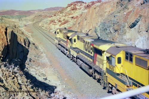 247-33
Near Cooya Pooya at the 37.5 km on the Robe River Cape Lambert line an empty train passes under the town water supply pipeline and pass through Lockyer Gap behind the standard Robe power of quad CM40-8M or Dash 8 locomotives led by 9425 which is a Goninan WA ALCo to GE rebuild CM40-8M with serial 6266-8 / 89-85 from August 1989 and was originally an AE Goodwin built M636 ALCo serial C-6041-4 new for Mt Newman Mining (later BHP Iron Ore) in April 1970 and numbered 5468, sold to Robe and delivered by road 17th August 1982, compare to second unit 9410 with a Comeng style large flat fuel tank. Location is [url=https://goo.gl/maps/nLyndU6bg2HA5SZX6]here[/url].22nd May 2002.
Keywords: 9410;Goninan;GE;CM40-8M;2160-03/96-202;rebuild;Comeng-NSW;ALCo;M636;C-6096-5;