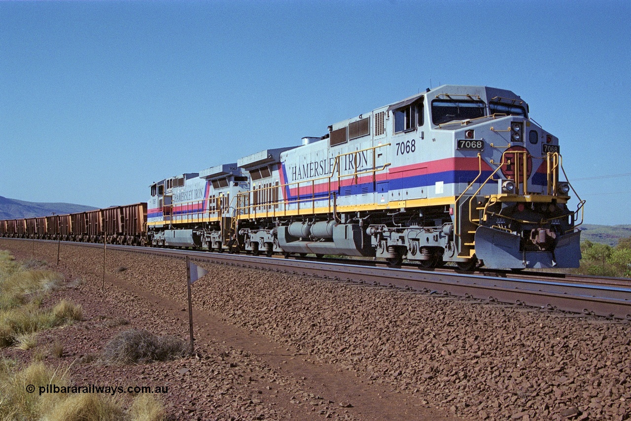 250-03
Pelican Siding on the Hamersley Iron Tom Price line about the 208 km with an empty train behind the standard pairing of two General Electric built 9-44CW units 7068 serial 47747 and 7067 serial 47746 stand on the loop or passing track for a meet with a loaded train. 21st October 2000.
Keywords: 7068;GE;Dash-9-44CW;47747;