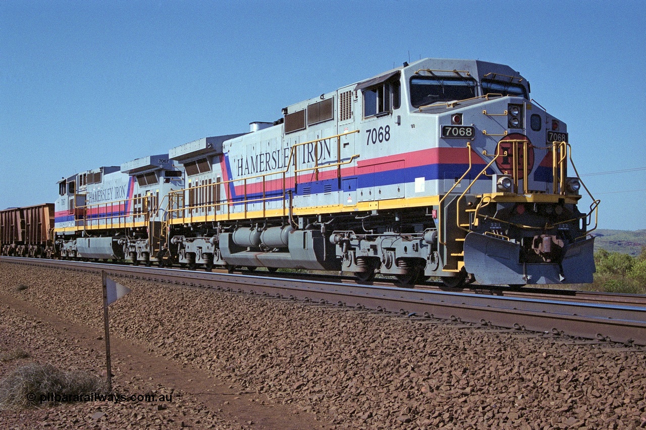 250-04
Pelican Siding on the Hamersley Iron Tom Price line about the 208 km with an empty train behind the standard pairing of two General Electric built 9-44CW units 7068 serial 47747 and 7067 serial 47746 stand on the loop or passing track for a meet with a loaded train. 21st October 2000.
Keywords: 7068;GE;Dash-9-44CW;47747;