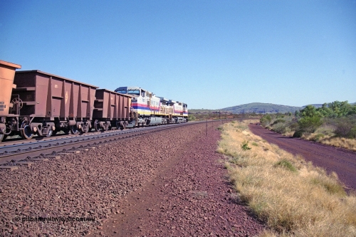 250-09
Pelican Siding on the Hamersley Iron Tom Price line about the 208 km with an empty train behind the standard pairing of two General Electric built 9-44CW units 7068 serial 47747 and 7067 serial 47746 stand on the loop or passing track for a meet with a loaded train. 21st October 2000.
