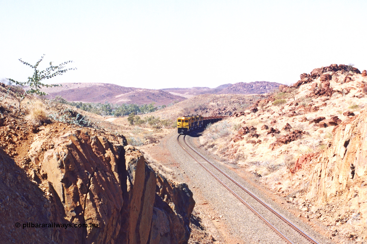 283-29
Near Woodbrook as the train rounds the curve just north of the 38.5 km grade crossing and through the cutting that will see it pass under the water pipe bridge behind the quad Robe River CM40-8M working of 9414, 9420, 9410 and 9525 with 202 waggons bound for Cape Lambert. 22nd of May 2002.
