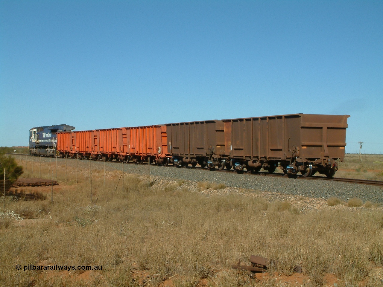 040806 091122
Goldsworthy Junction, trailing view of the weighbridge test train with the four orange weighbridge test waggons and one of the two Comeng built ore waggons to provide braking, 5666 is the power.
