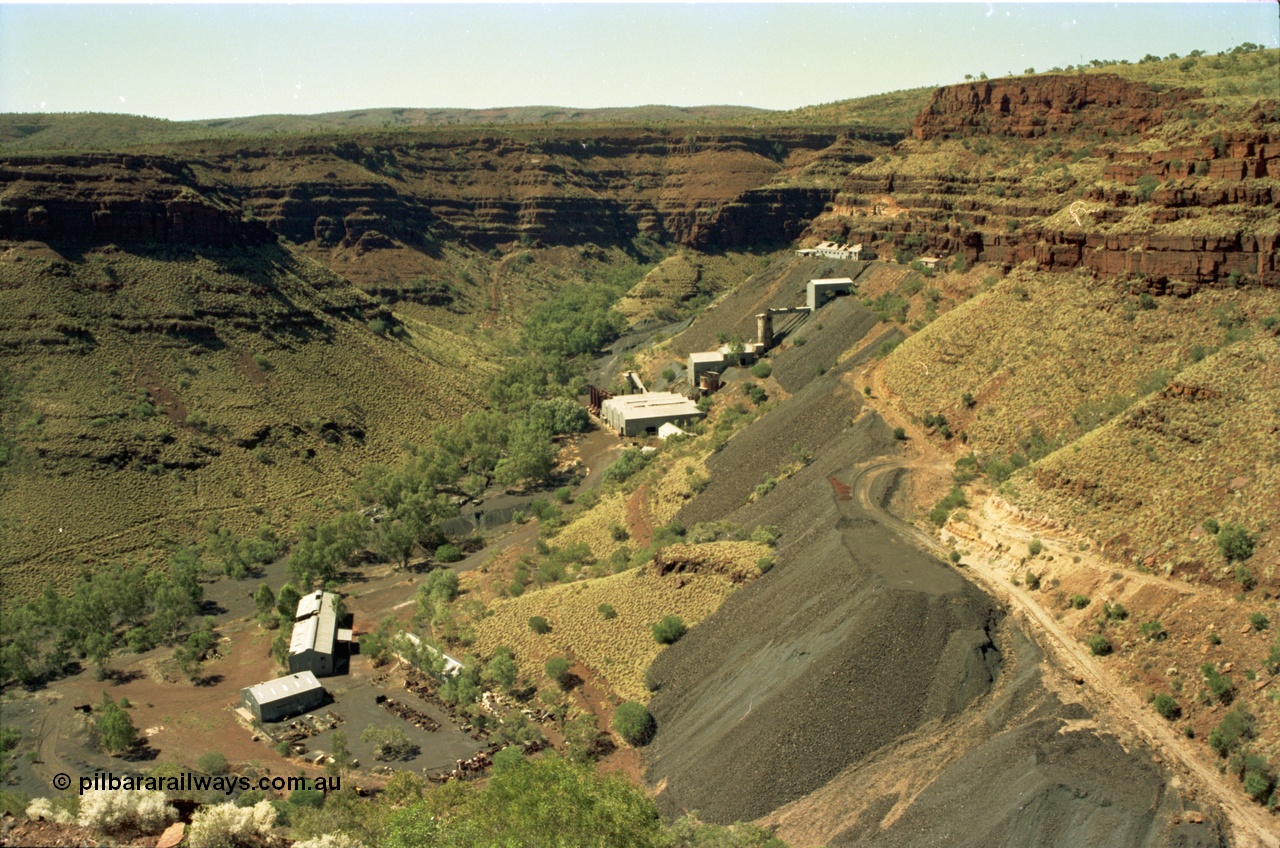 195-15
Wittenoom, view from the Devil's Staircase of Colonial Mill and Mine with piles of tailings, the building and yard at the bottom of the frame is the warehouse or store and gated yard with the workshop being the larger of the two, the buildings at the top level are the locomotive and underground mining offices and workshops, with the crusher and milling and bagging plant using gravity to its advantage.
