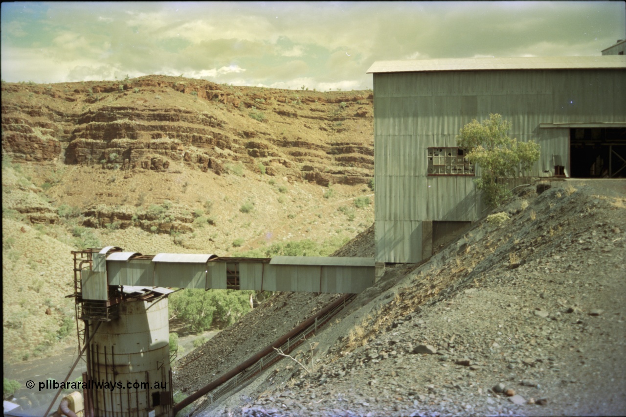 195-36
Wittenoom Gorge, Australian Blue Asbestos or ABA Colonial Mill, view of primary crushing building, shows conveyor housing and silo structure with piping and a steep stair walkway from the lower levels to the crushing shed.
