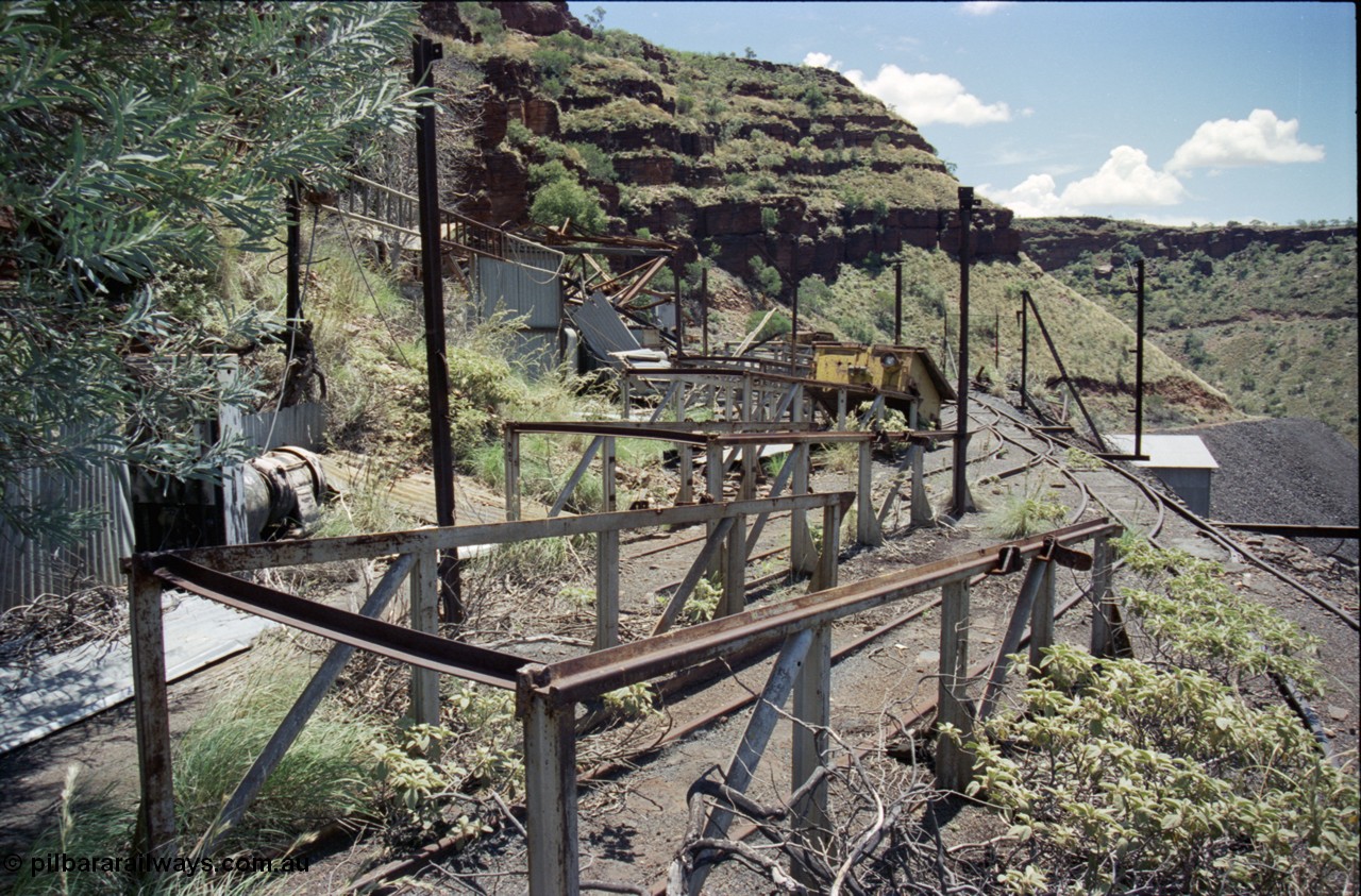 197-11
Wittenoom, Colonial Mine, asbestos mining remains, view looking north from the 197-10 location at the remains of the battery charging shed with only post and the back wall intact, a battery charging MG-set is visible along with the battery off-take ramps and a battery module.
