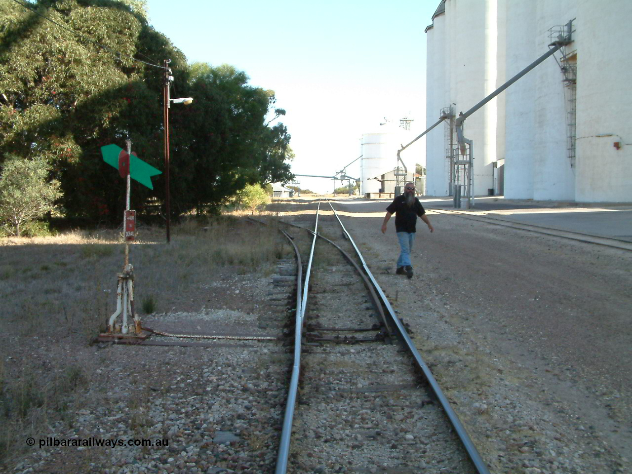 030405 155300
Lock, yard overview looking south, points and lever with indicator for the siding off the mainline, concrete silo complex Block 2 and outflow spout visible on the right as local identity Pope Searle wanders around the yard. 5th April 2003.
